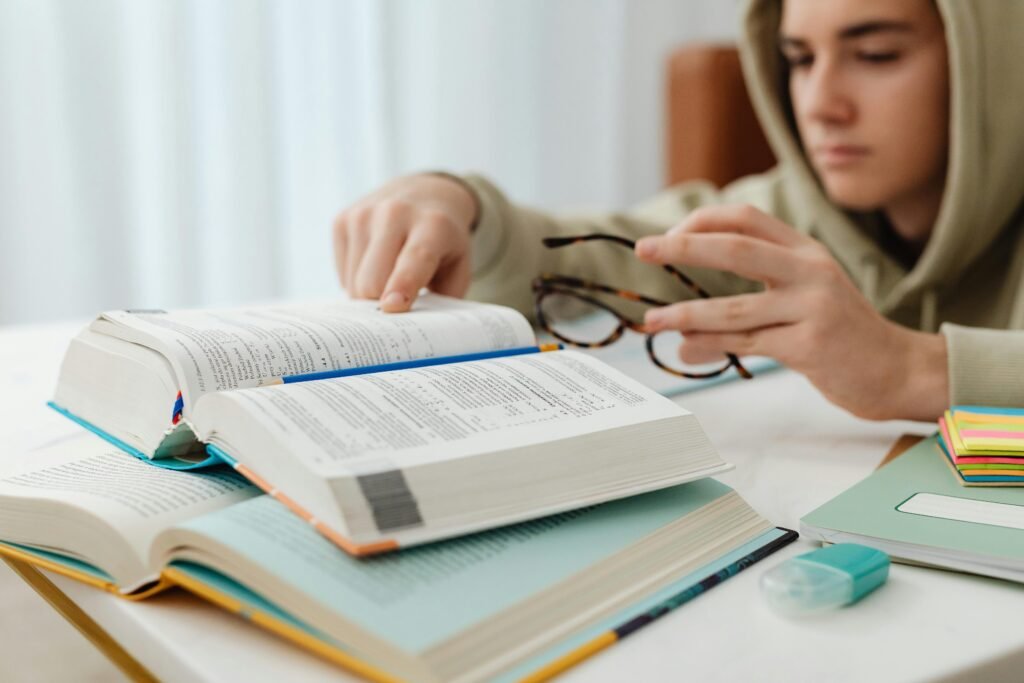Focused teenager studying with open textbooks, eyeglasses, and notes.